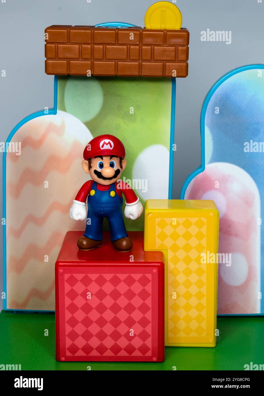 Super Mario debout sur une plate-forme carrée rouge avec un fond coloré derrière lui Banque D'Images