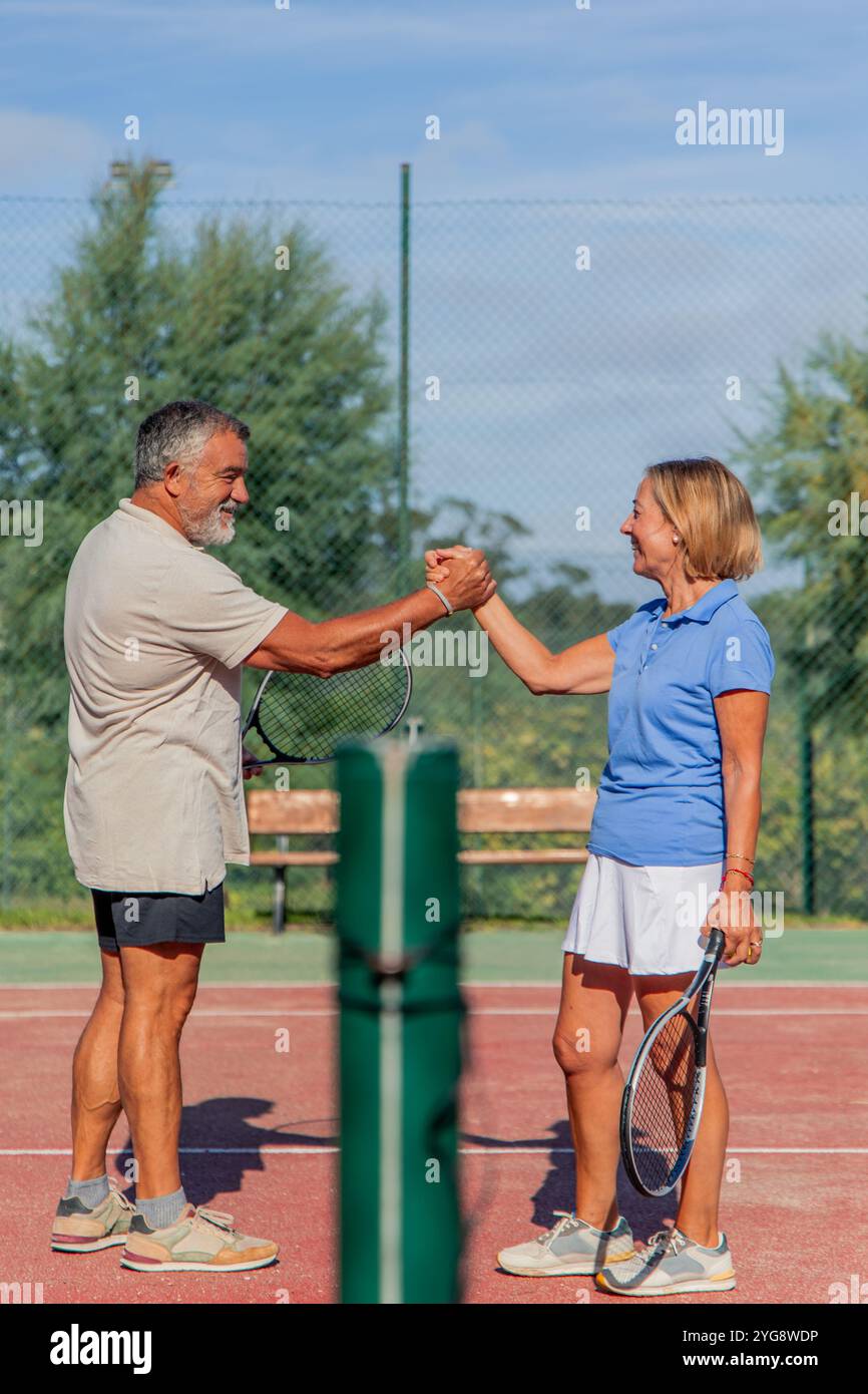 vertical avant leur match, un couple âgé de joueurs de tennis se salue avec une poignée de main amicale, les deux souriant chaleureusement. Le filet à l'arrière Banque D'Images