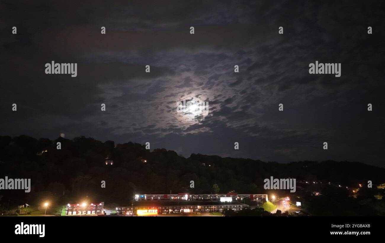 Regarder la lune à travers un voile de nuages couvrant le ciel nocturne révèle une scène sereine et mystique, avec un doux clair de lune filtrant à travers. Banque D'Images