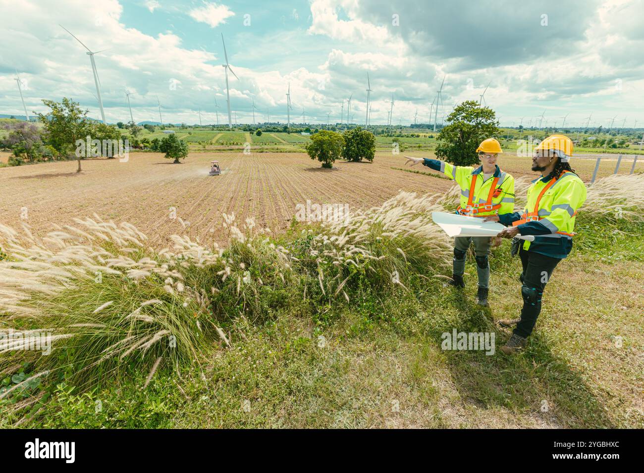 L'équipe d'ingénieurs mélange des ouvriers noirs et blancs masculins avec le plan d'étage à l'étude de travail sur le terrain de turbines éoliennes sur le terrain de ferme de générateur d'électricité éolienne en plein air. Banque D'Images