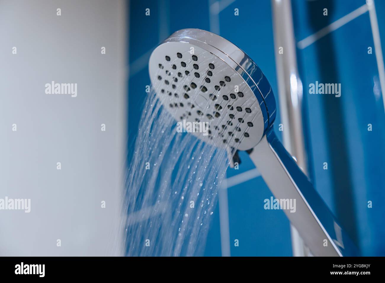 Gros plan propre Nouveau Chrome Shiny Wet Watering Flow pomme de douche dans le fond de mur bleu de salle de bains Banque D'Images
