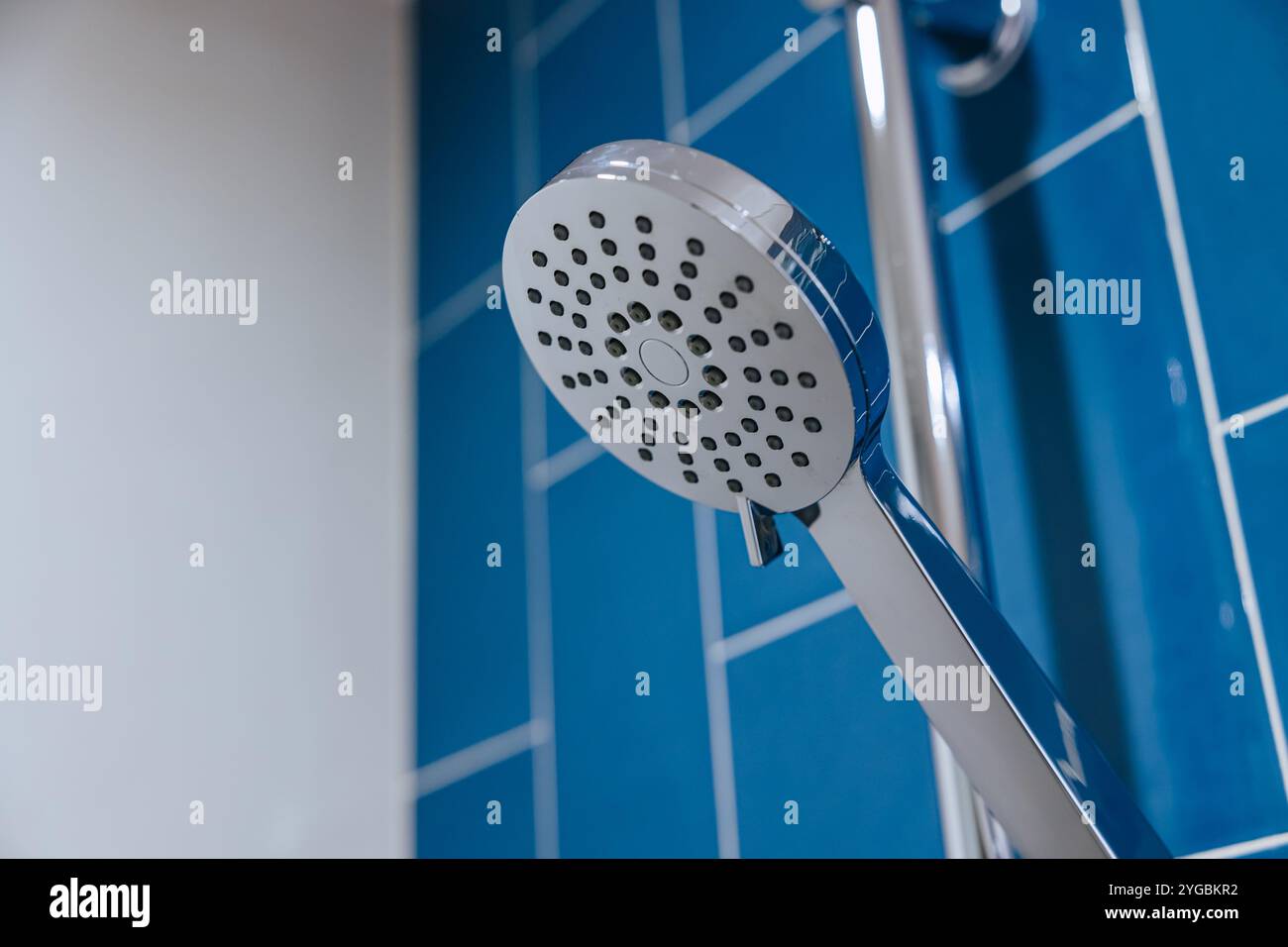 Gros plan propre Nouvelle pomme de douche sèche brillante chromée dans le fond de mur bleu de salle de bains Banque D'Images