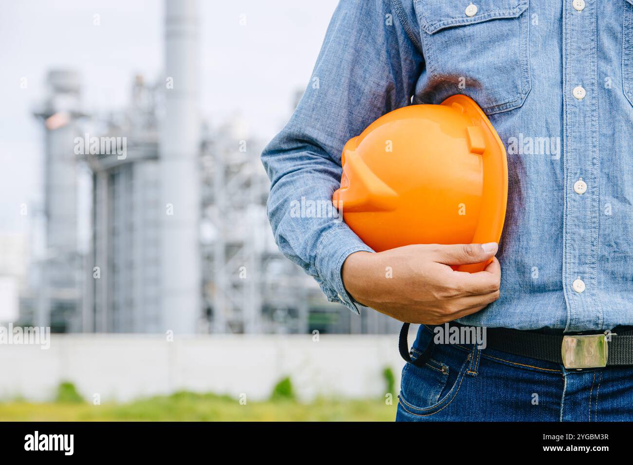 Ingénieur professionnel homme travaillant debout contre le bâtiment de l'industrie de raffinerie de gaz de pétrole gros plan main tenant casque de sécurité. Banque D'Images