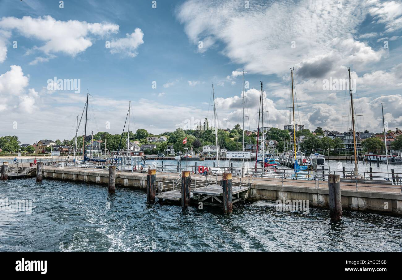 Une scène portuaire pittoresque avec des voiliers amarrés au quai, sous un ciel bleu vibrant avec des nuages éparpillés. L'eau tranquille et la ville pittoresque enhan Banque D'Images