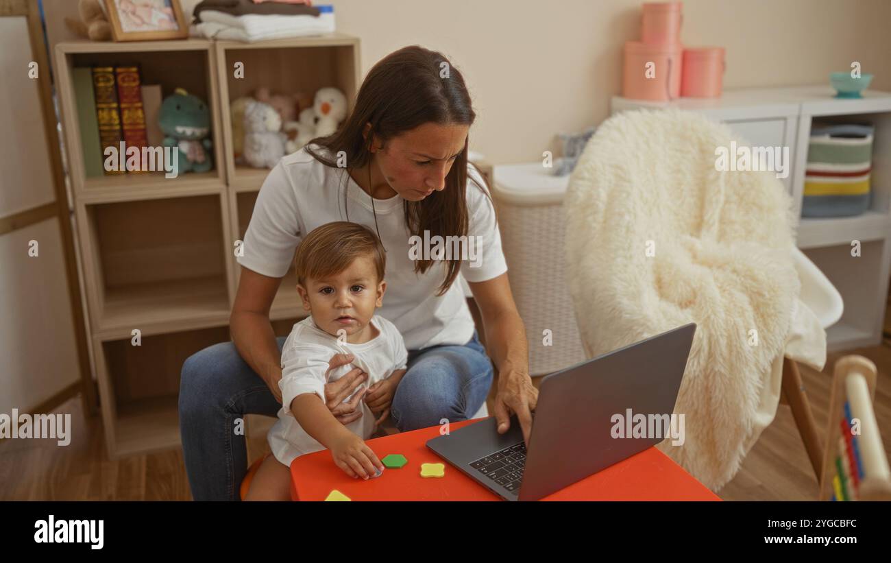 Femme avec fils à l'aide d'un ordinateur portable dans une salle de jeux confortable de la maternelle, entourée de jouets et de décor, représentant une scène de famille à l'intérieur avec une attention et une interactivité Banque D'Images