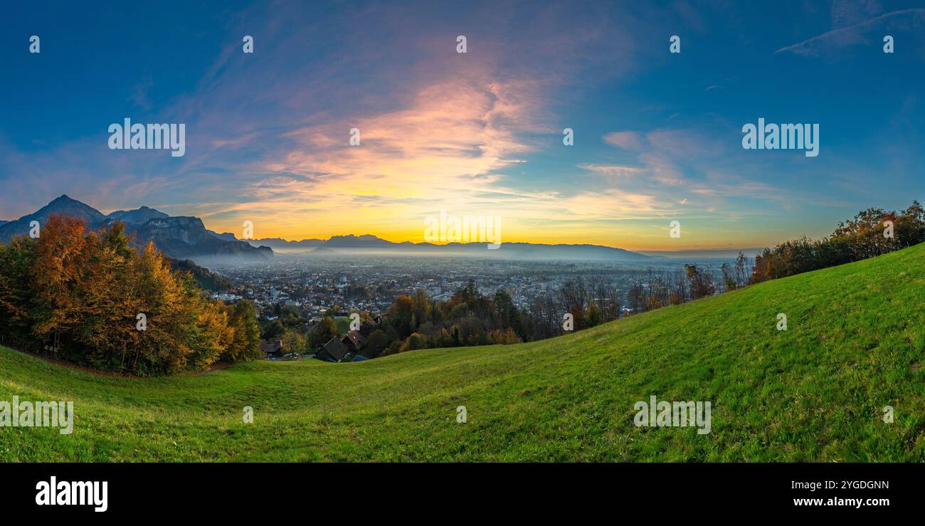 Panorama coucher de soleil dans la vallée du Rhin, avec rémanence, ciel bleu sur la ville de Dornbirn, prairie et champs. arbres colorés d'automne. belle récréation Banque D'Images