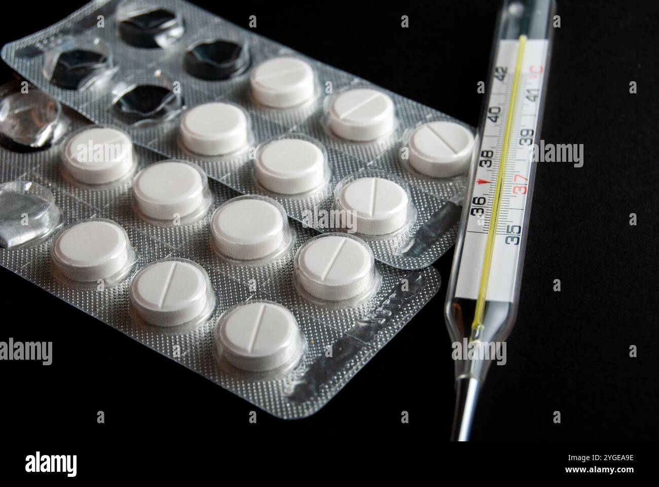 Gros plan du thermomètre et des pilules de paracétamol isolés sur le fond noir. Banque D'Images