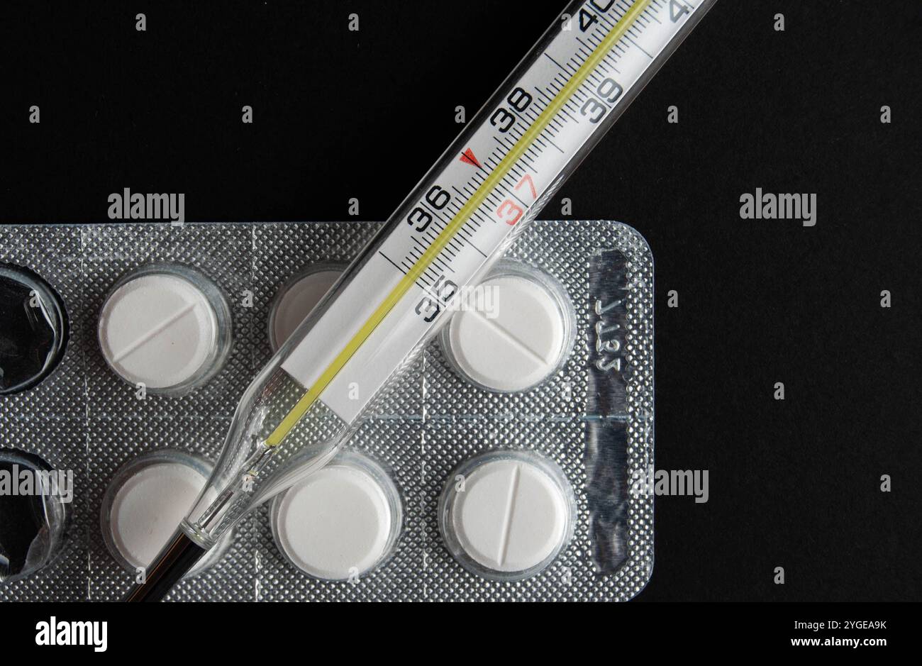 Image détaillée de pilules de paracétamol avec un thermomètre, mettant l'accent sur les soins de santé et le traitement du rhume / grippe, sur un fond sombre et contrasté. Banque D'Images