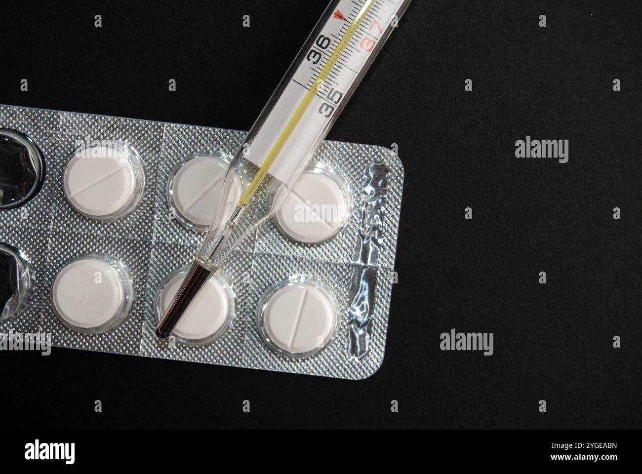 Gros plan d'un thermomètre et de pilules de paracétamol isolés sur fond noir, idéal pour illustrer la santé, la médecine et la grippe saisonnière. Banque D'Images