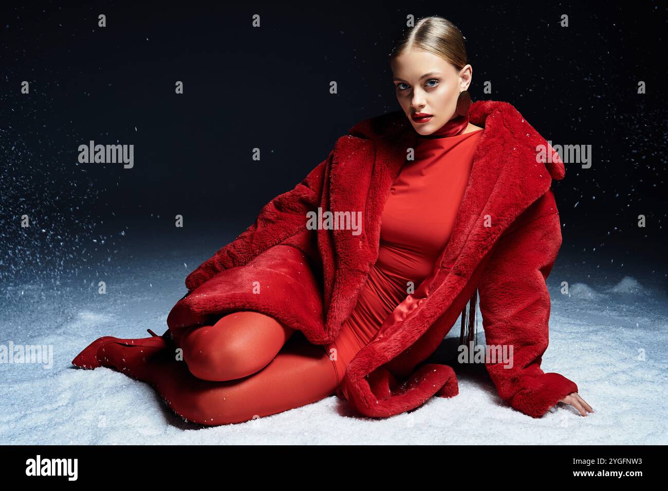 Une jeune femme étonnante s'assoit élégamment sur la neige, mettant en valeur sa tenue rouge éclatante avec calme. Banque D'Images