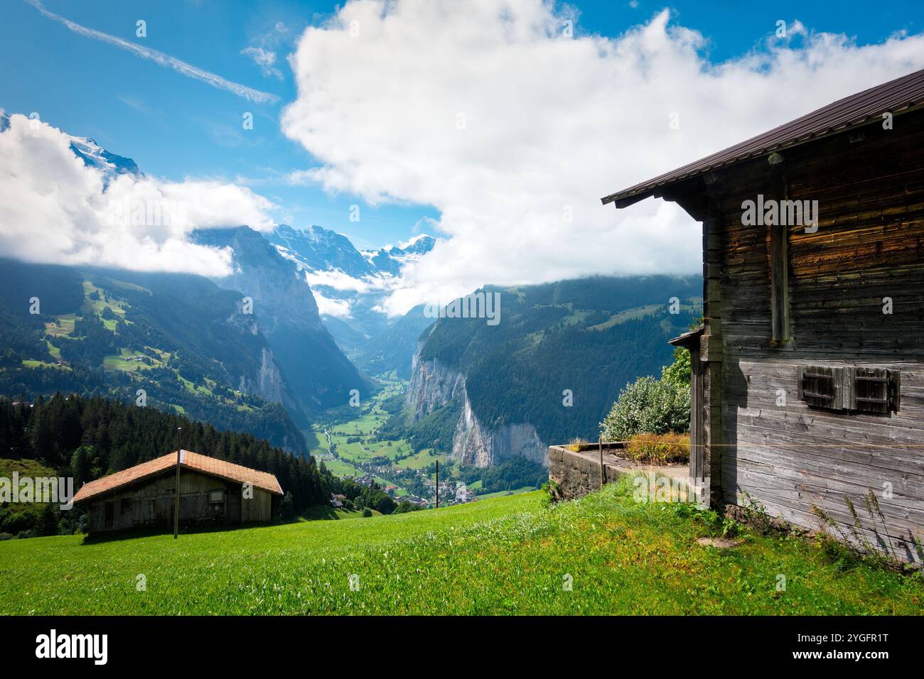 Paysage avec deux maisons de chalet en bois avec vue sur la vallée de Lauterbrunnen entourée de hautes montagnes des Alpes, vu de Wengen en Suisse. Banque D'Images