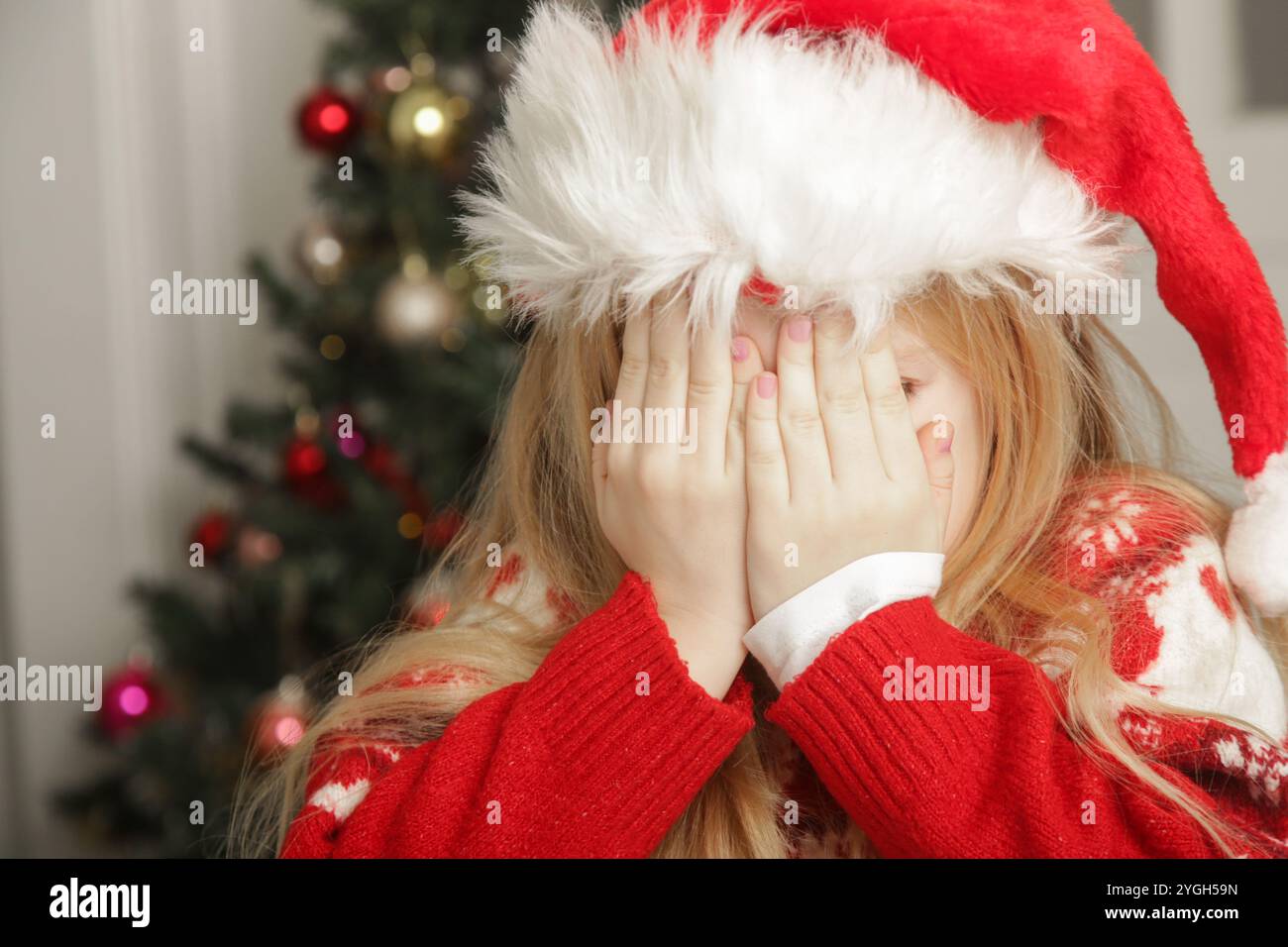 Petite fille triste et frustrée dans la tenue de Noël et chapeau de Père Noël assis à la table avec des biscuits de pain d'épices, concept de stress de vacances d'hiver. Banque D'Images