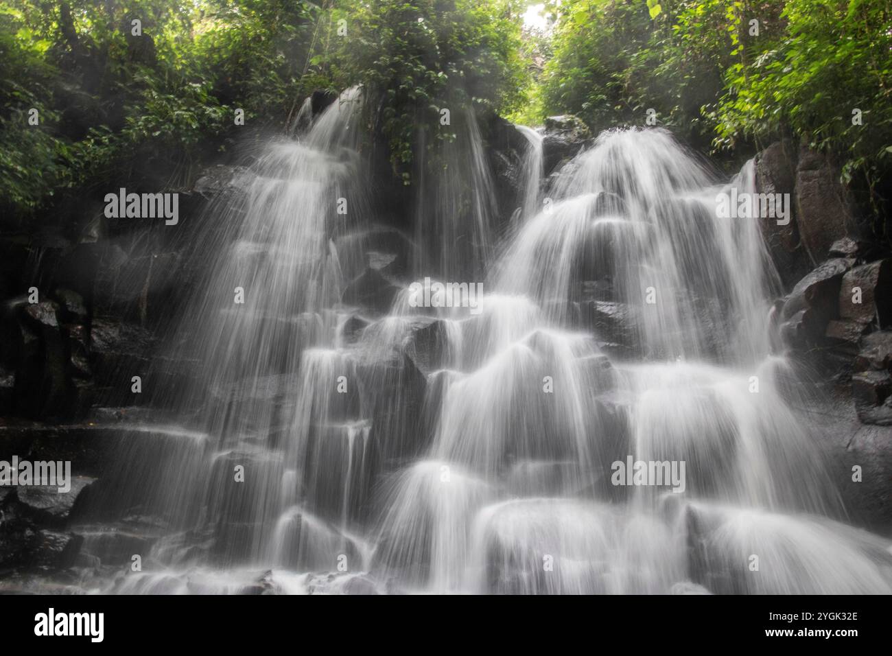 Belle cascade cachée qui tombe sur plusieurs niveaux, entourée de roche de lave noire Kanto Lampo, Bali, Indonésie Banque D'Images