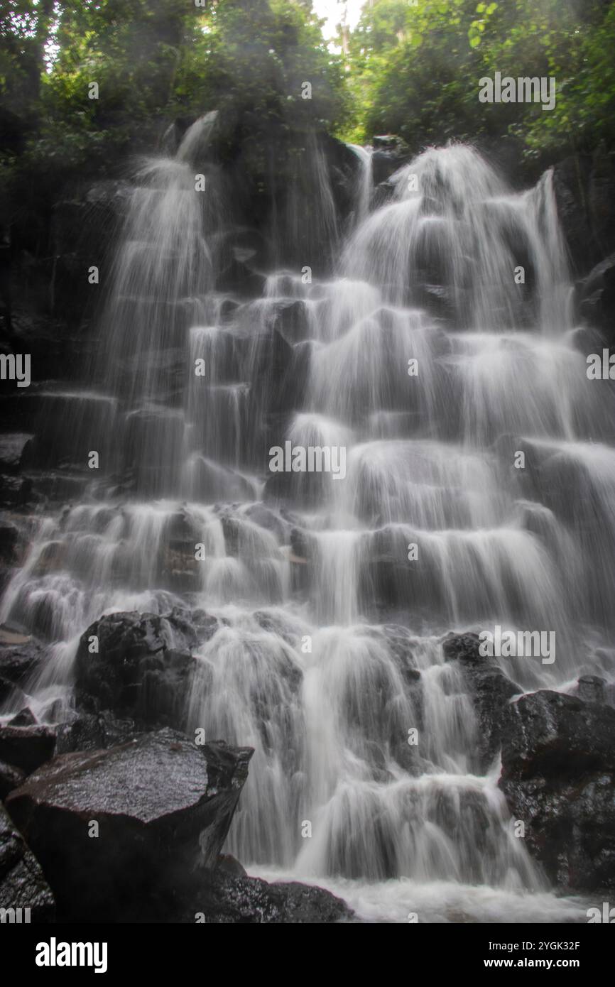 Belle cascade cachée qui tombe sur plusieurs niveaux, entourée de roche de lave noire Kanto Lampo, Bali, Indonésie Banque D'Images