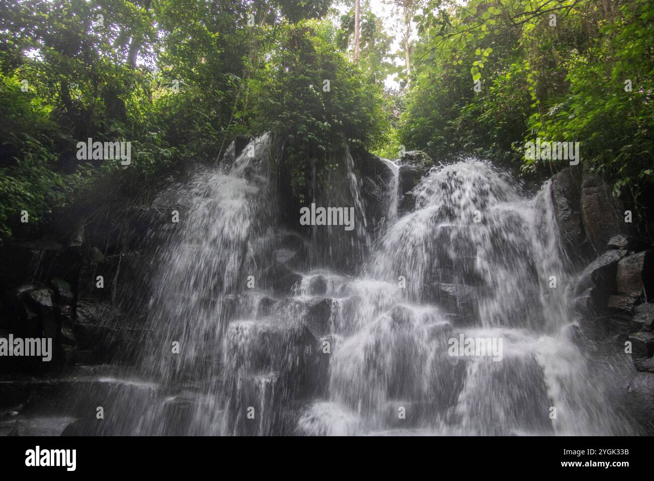 Belle cascade cachée qui tombe sur plusieurs niveaux, entourée de roche de lave noire Kanto Lampo, Bali, Indonésie Banque D'Images
