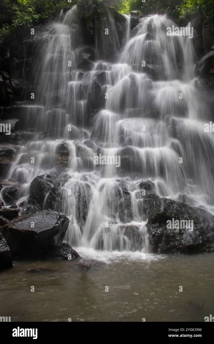 Belle cascade cachée qui tombe sur plusieurs niveaux, entourée de roche de lave noire Kanto Lampo, Bali, Indonésie Banque D'Images