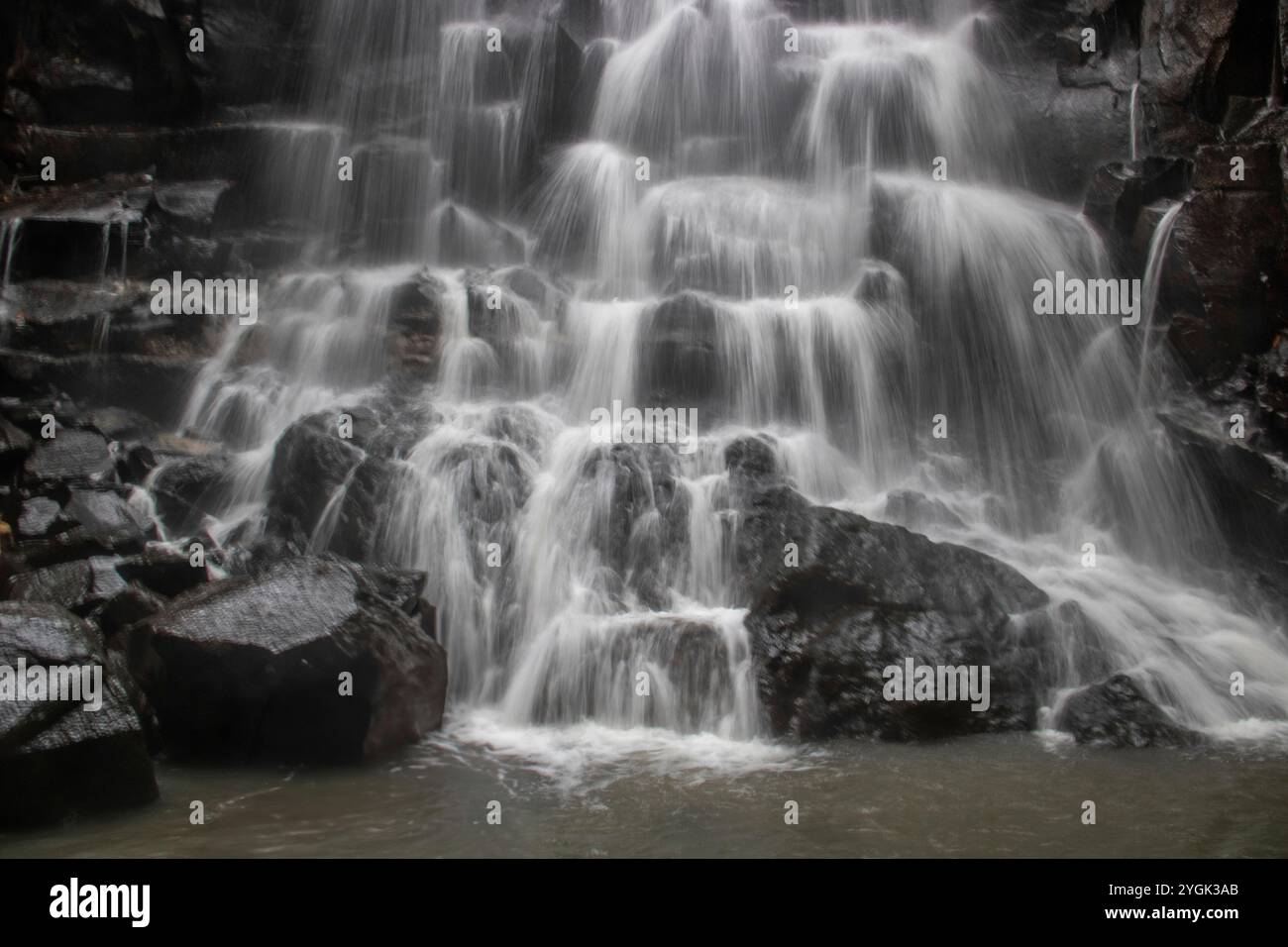 Belle cascade cachée qui tombe sur plusieurs niveaux, entourée de roche de lave noire Kanto Lampo, Bali, Indonésie Banque D'Images