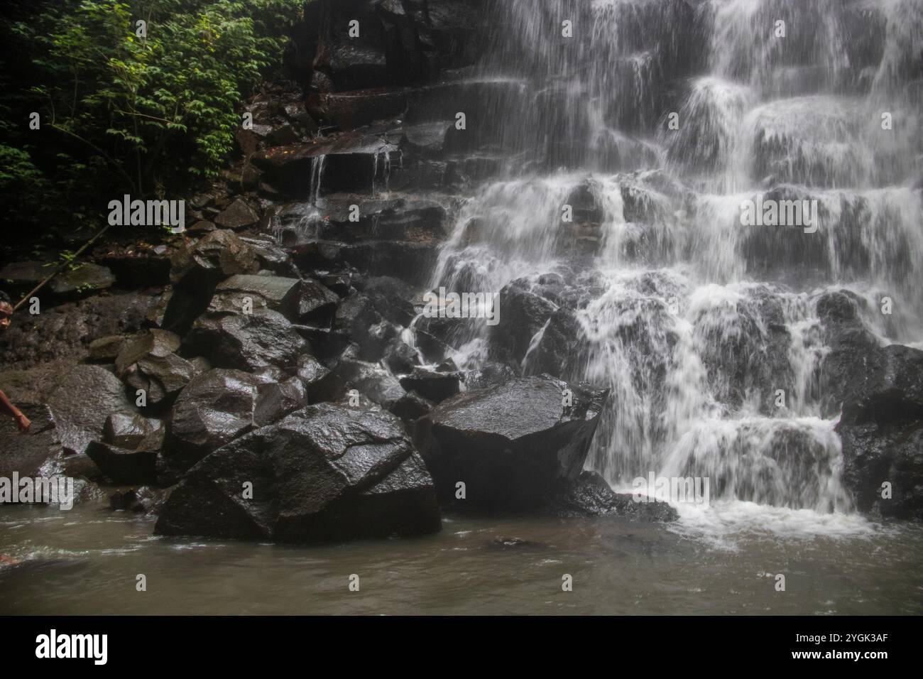 Belle cascade cachée qui tombe sur plusieurs niveaux, entourée de roche de lave noire Kanto Lampo, Bali, Indonésie Banque D'Images