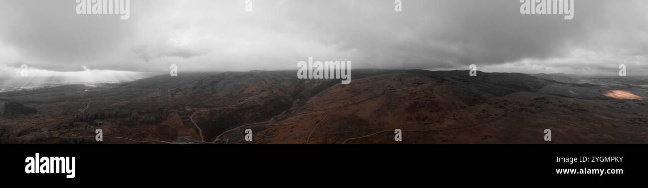 Paysage panoramique Moody sous de lourds nuages, avec des taches de lumière du soleil se perçant, projetant des ombres dramatiques sur le terrain accidenté en contrebas. Banque D'Images