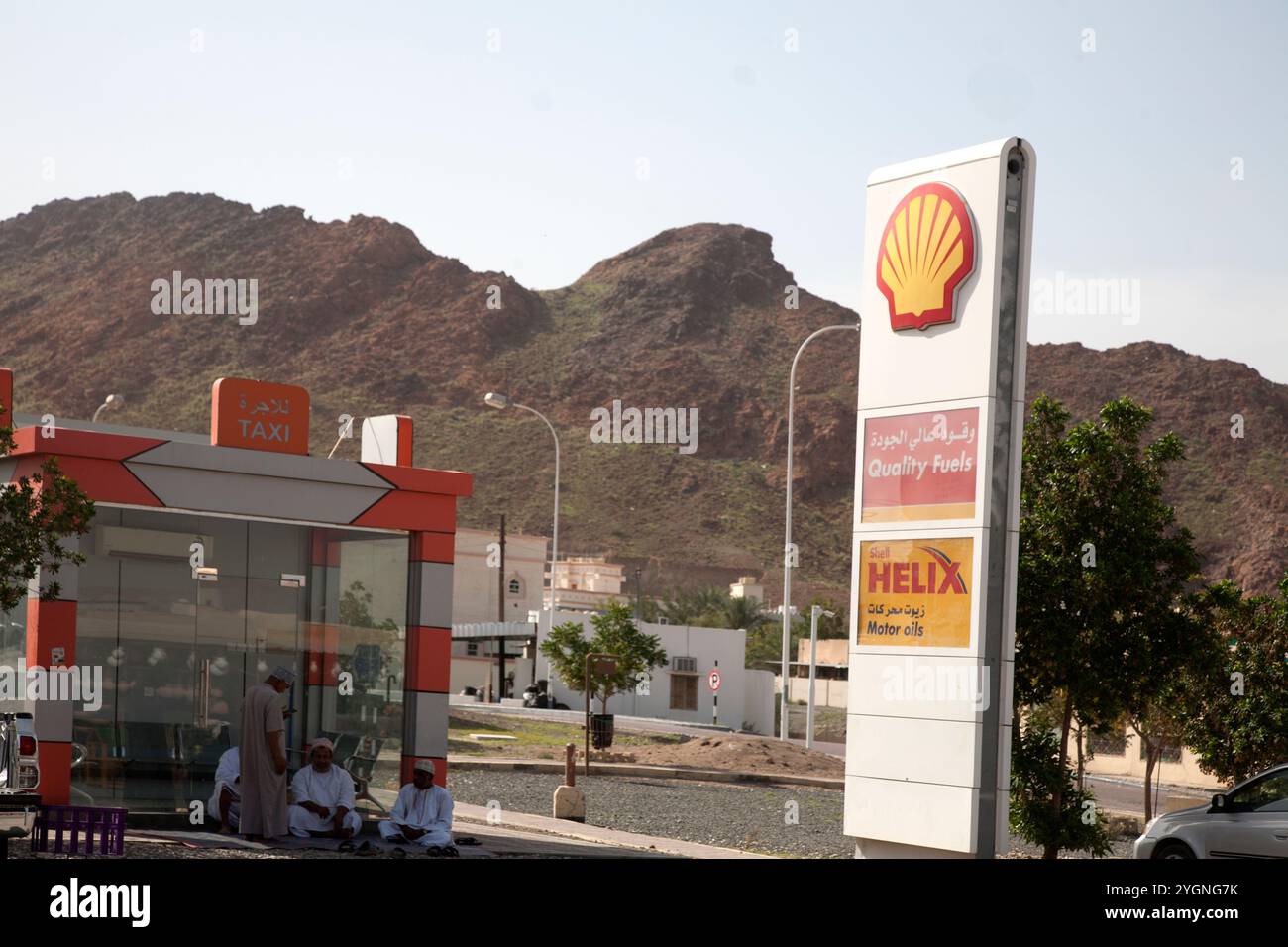 omni hommes assis sur le sol au point de ramassage de taxi par shell station-service fanja oman moyen-orient Banque D'Images