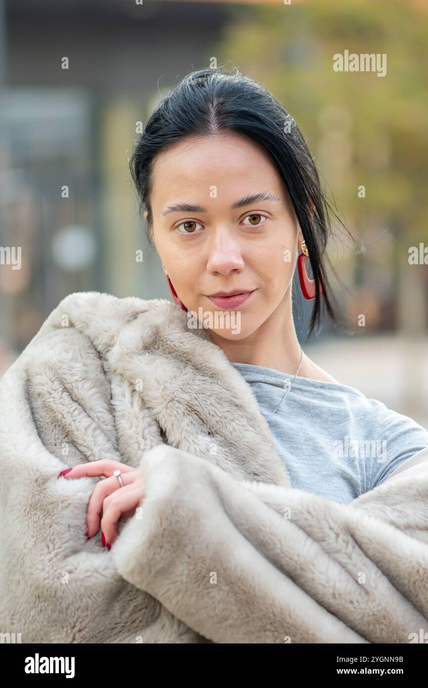 Une jeune femme de 20-25 ans se tient dans un quartier urbain, avec de longs cheveux noirs et des boucles d'oreilles élégantes, exsudant la confiance et regardant directement dans Banque D'Images