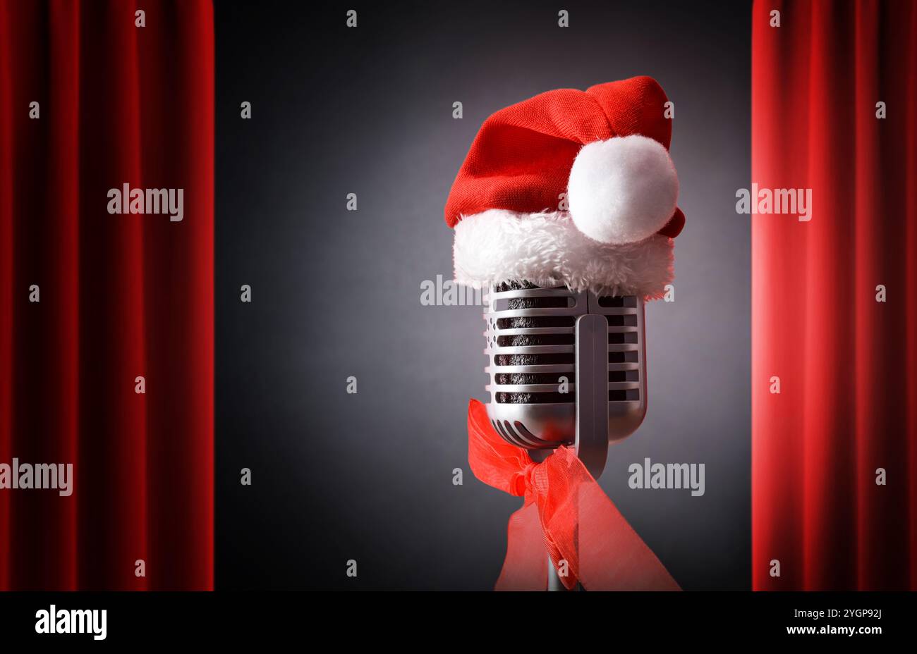 Spectacle de divertissement de Noël avec microphone rétro avec chapeau de Père Noël illuminé par un faisceau de lumière sur scène avec des rideaux rouges ouverts et dos noir Banque D'Images