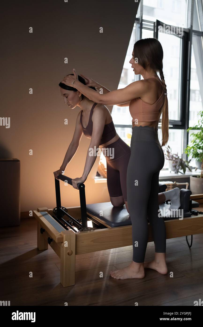 Femme formant pilates sur le lit reformer avec entraîneur. Machine studio Reformer Pilates pour les séances d'entraînement en salle de gym. Forme, saine et forte Banque D'Images