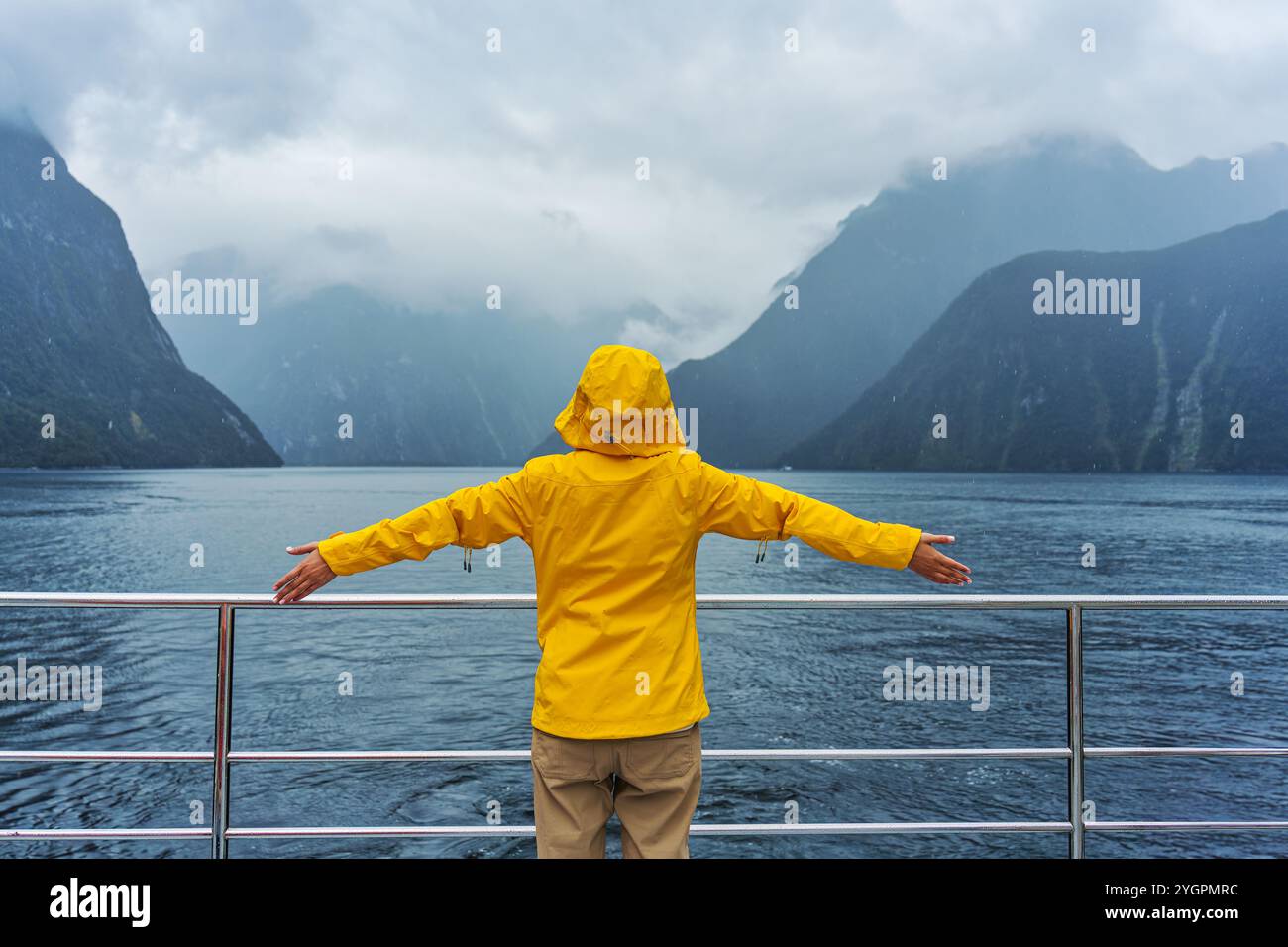 Heureuse femme touristique en veste jaune profitant de la vue sur Milford Sound pendant la croisière en ferry en vacances au parc national Fiord, Nouvelle-Zélande Banque D'Images