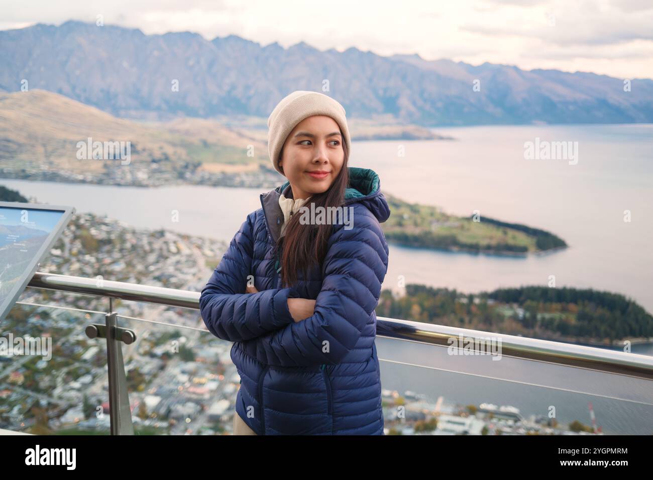 Heureuse femme asiatique en veste duvet debout au point de vue sur Queenstown, Nouvelle-Zélande Banque D'Images