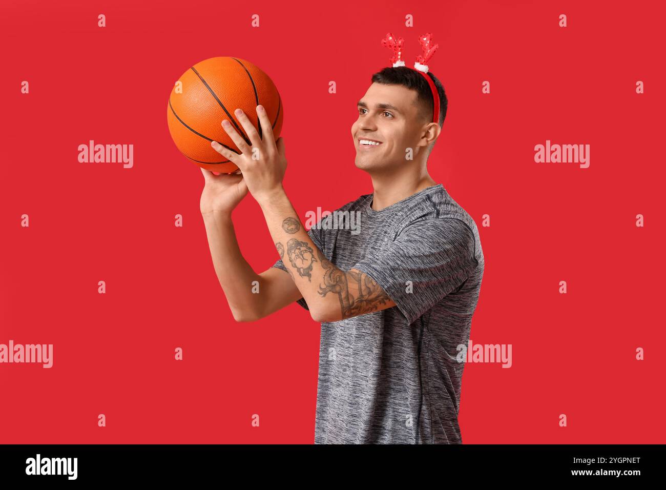 Jeune homme heureux dans des cornes de renne jouant au basket-ball sur fond rouge Banque D'Images