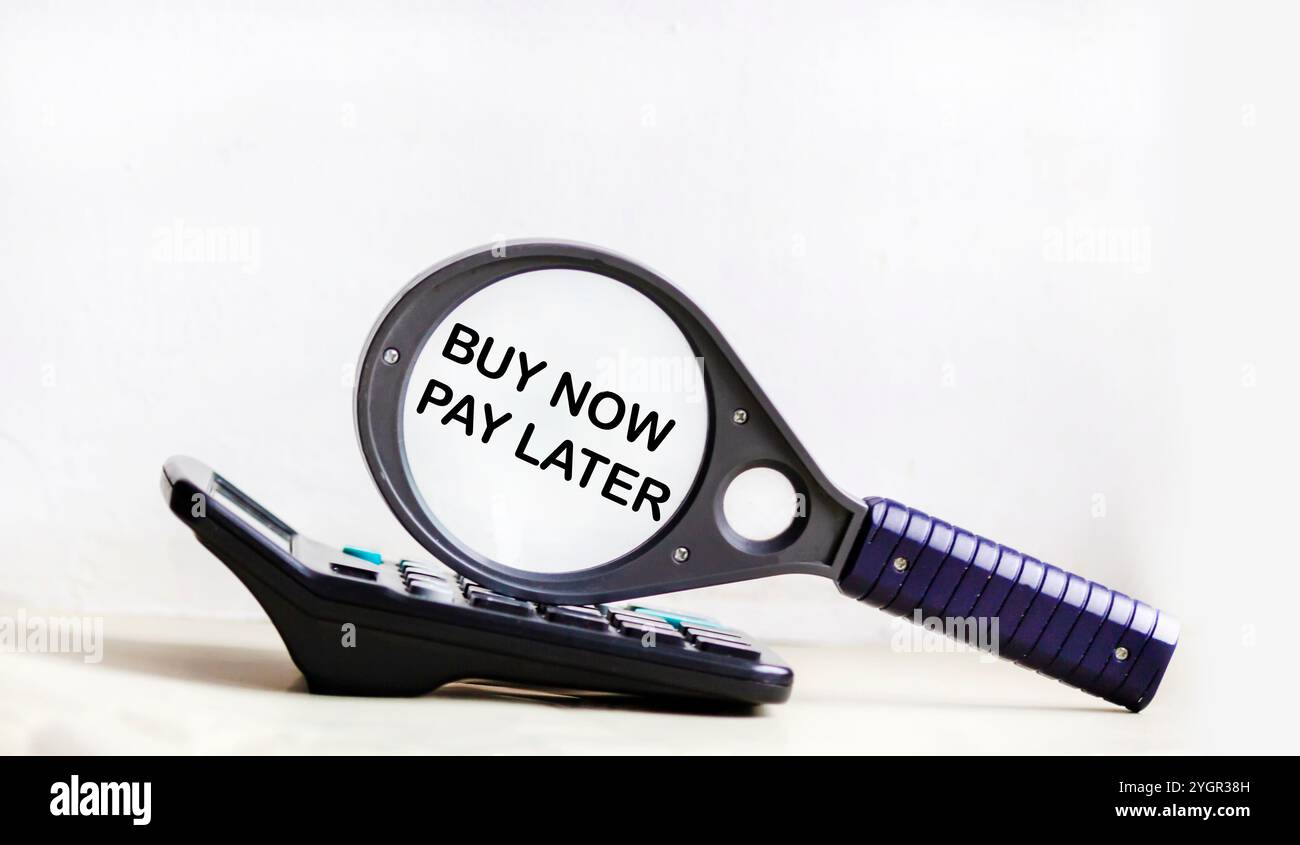 Concept financier et commercial. Sur fond blanc se trouve une calculatrice et une loupe avec l'inscription - ACHETER MAINTENANT PAYER PLUS TARD Banque D'Images