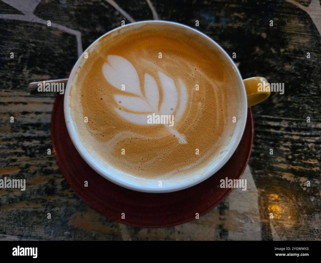 Café confortable avec arbre latte art dans la tasse jaune et soucoupe rouge sur la table en bois prise d'en haut avec cuillère sur le côté - Image de stock capturée avec un smartphone