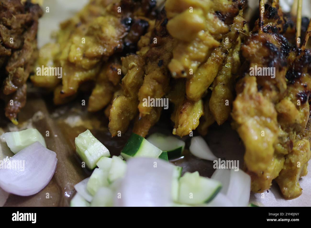 Gros plan de brochettes satay de poulet grillé servies avec une riche sauce aux arachides, du concombre frais et des tranches d'oignon. Banque D'Images