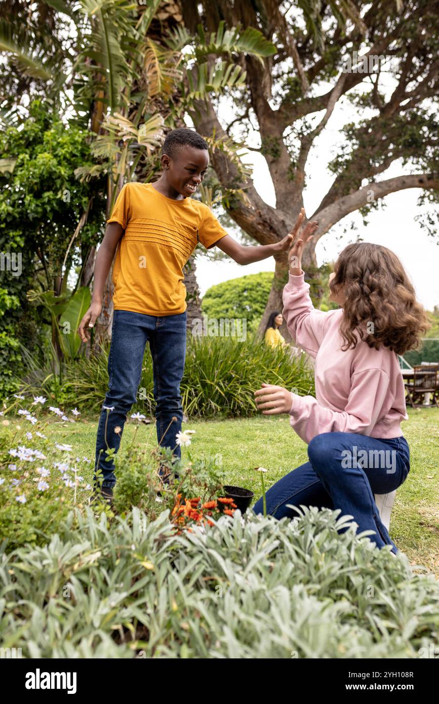enfants multiraciaux en haut-fiving dans le jardin, appréciant le travail d'équipe et le plaisir en plein air ensemble Banque D'Images