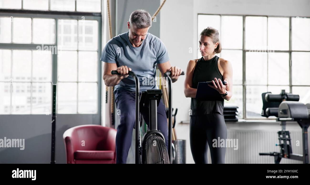 Entraînement cardio dans la salle de gym sur machine elliptique vélo avec entraîneur personnel Banque D'Images