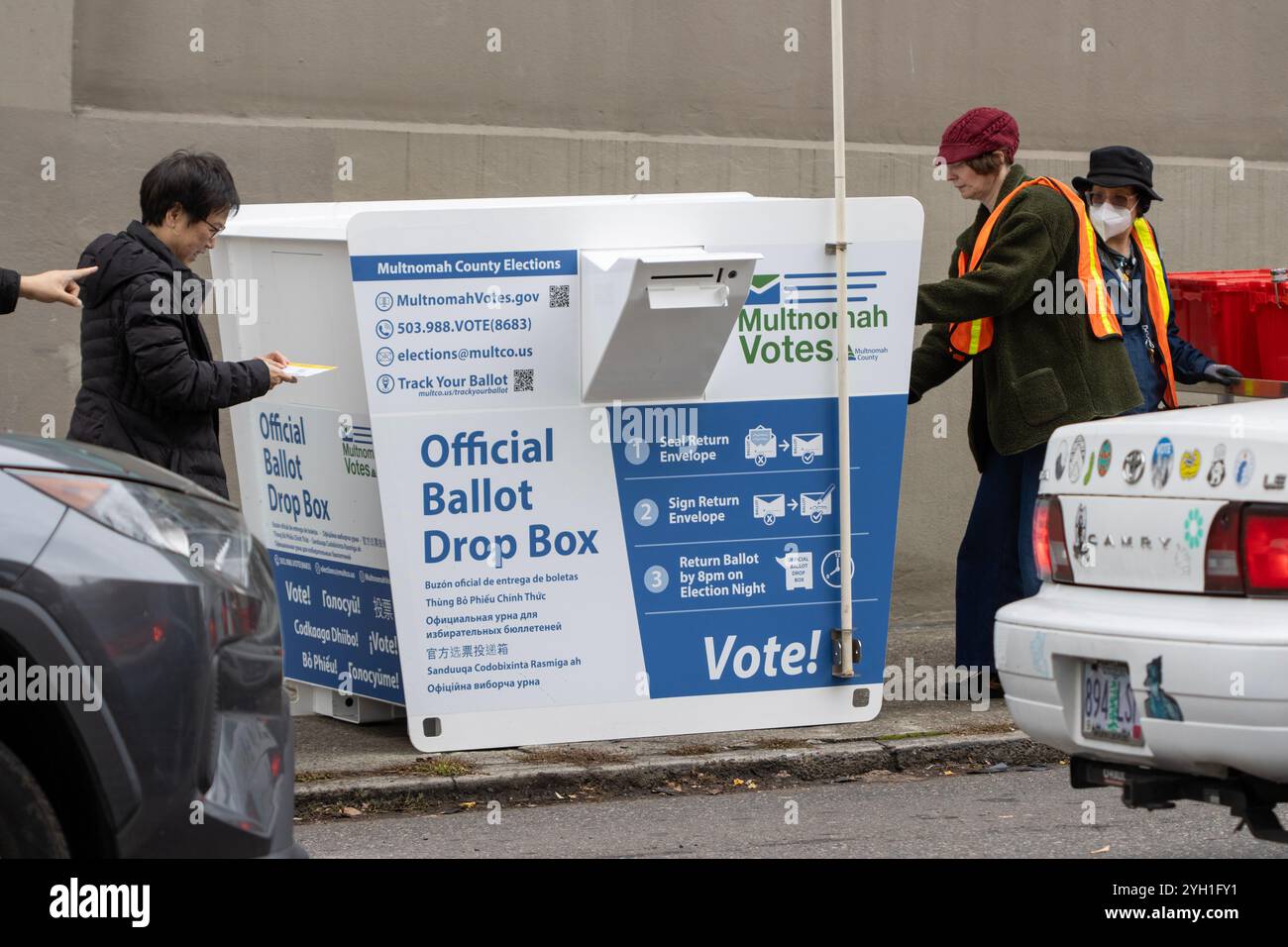 Les électeurs et les employés du bureau d'inscription des électeurs à une boîte de dépôt des bulletins de vote sur le trottoir à l'extérieur de la division électorale du comté de Multnomah à Portland... Banque D'Images