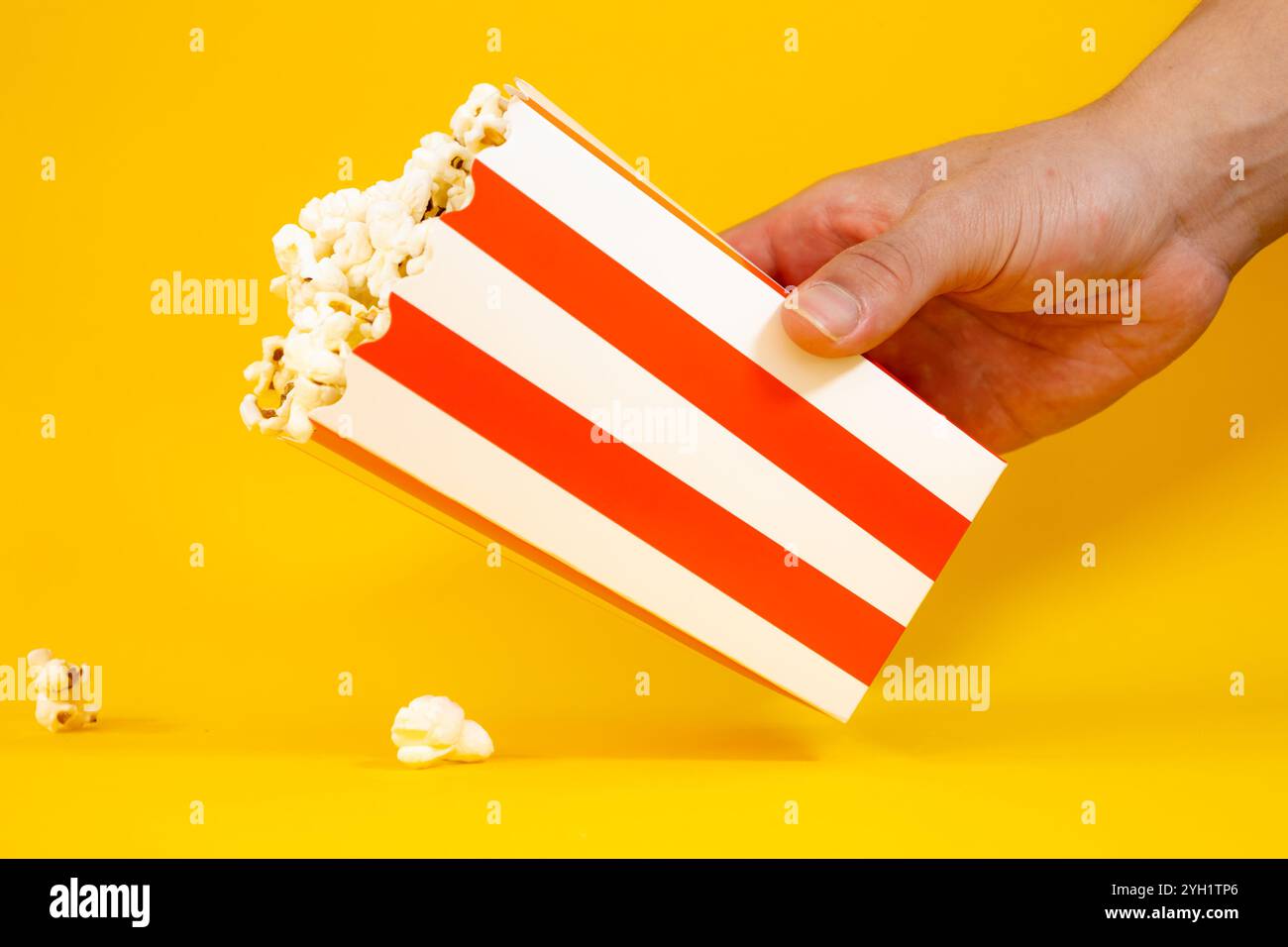 Main masculine tenant un seau en carton rouge et blanc avec pop-corn sur fond jaune, concept de pop-corn Banque D'Images