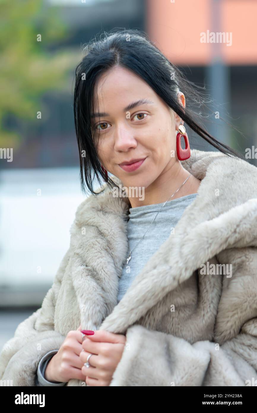 Portrait de rue d'une jeune femme élégante d'apparence orientale, 20-25 ans, sur fond de contours flous d'une ville européenne Banque D'Images