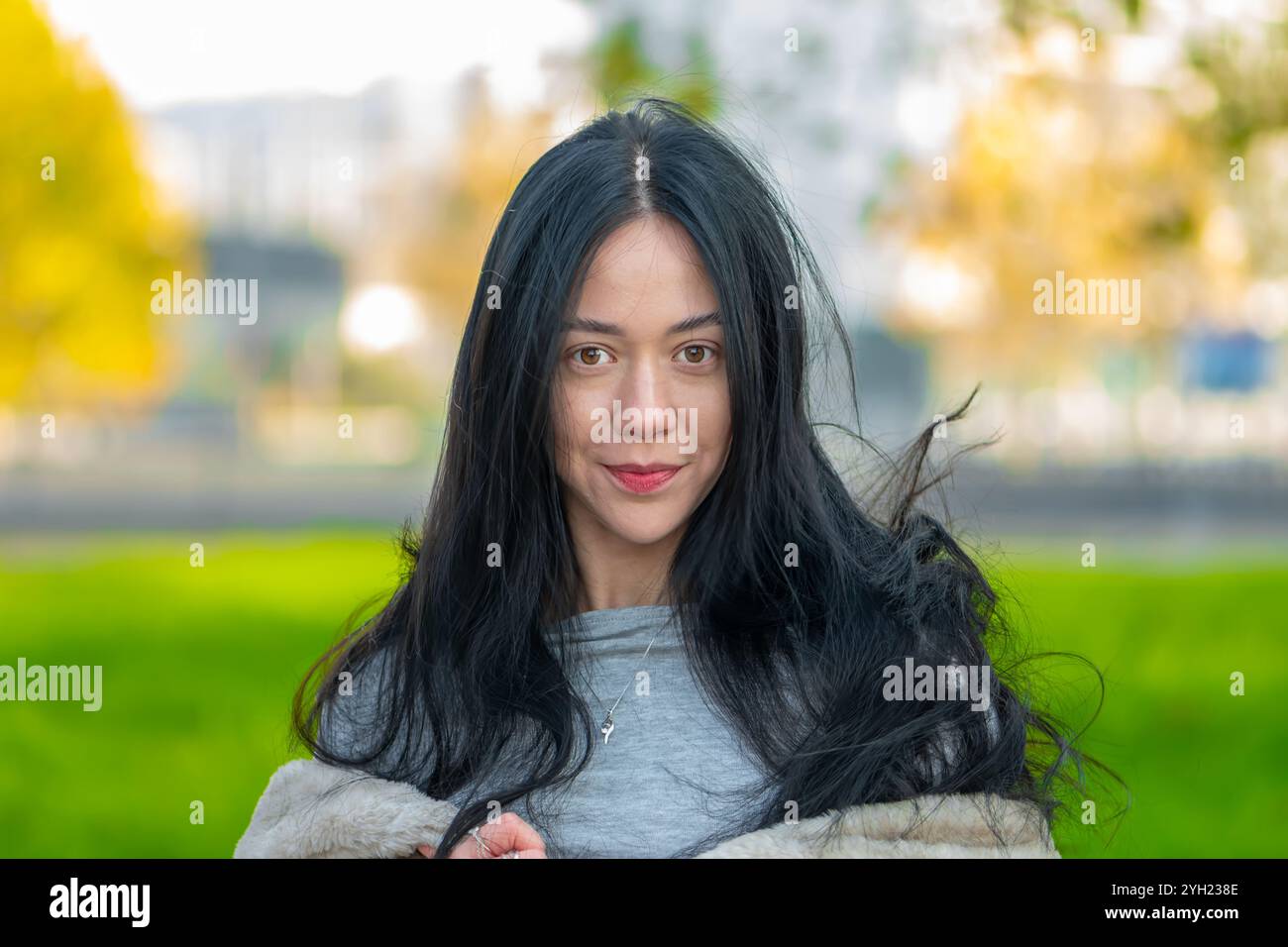 Une jeune femme de 20-25 ans se tient dans un quartier urbain, avec de longs cheveux noirs et des boucles d'oreilles élégantes, exsudant la confiance et regardant directement dans Banque D'Images