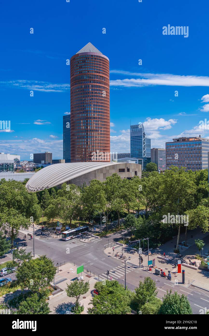 Un gratte-ciel saisissant présente une architecture contemporaine, entouré de verdure luxuriante et d'autres bâtiments, assis contre un ciel bleu clair pendant la journée Banque D'Images