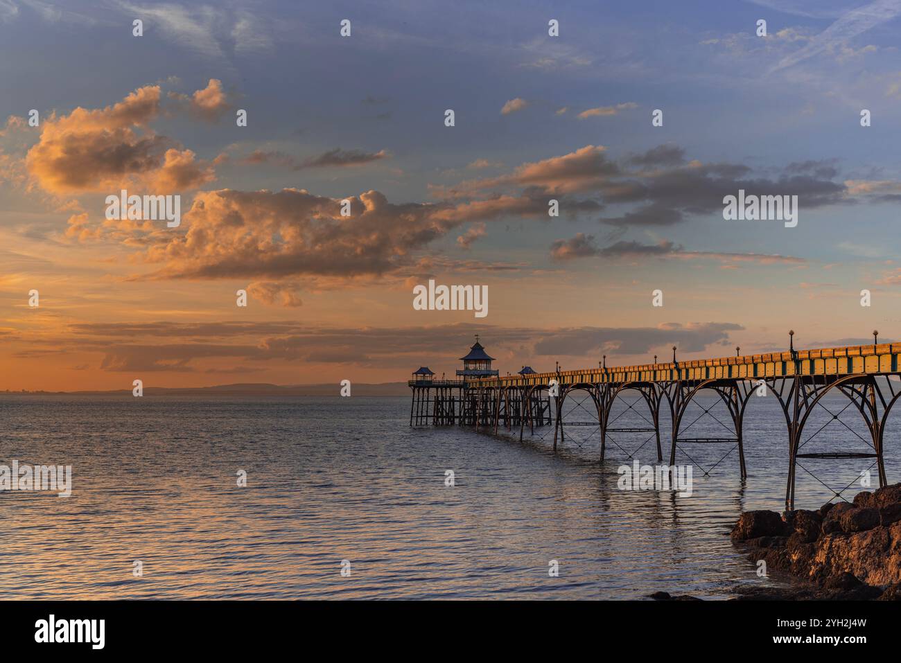 Clevedon Pier au coucher du soleil avec une couverture nuageuse et un ciel bleu avec la lumière du soleil se reflétant sur les panneaux latéraux de la jetée Banque D'Images