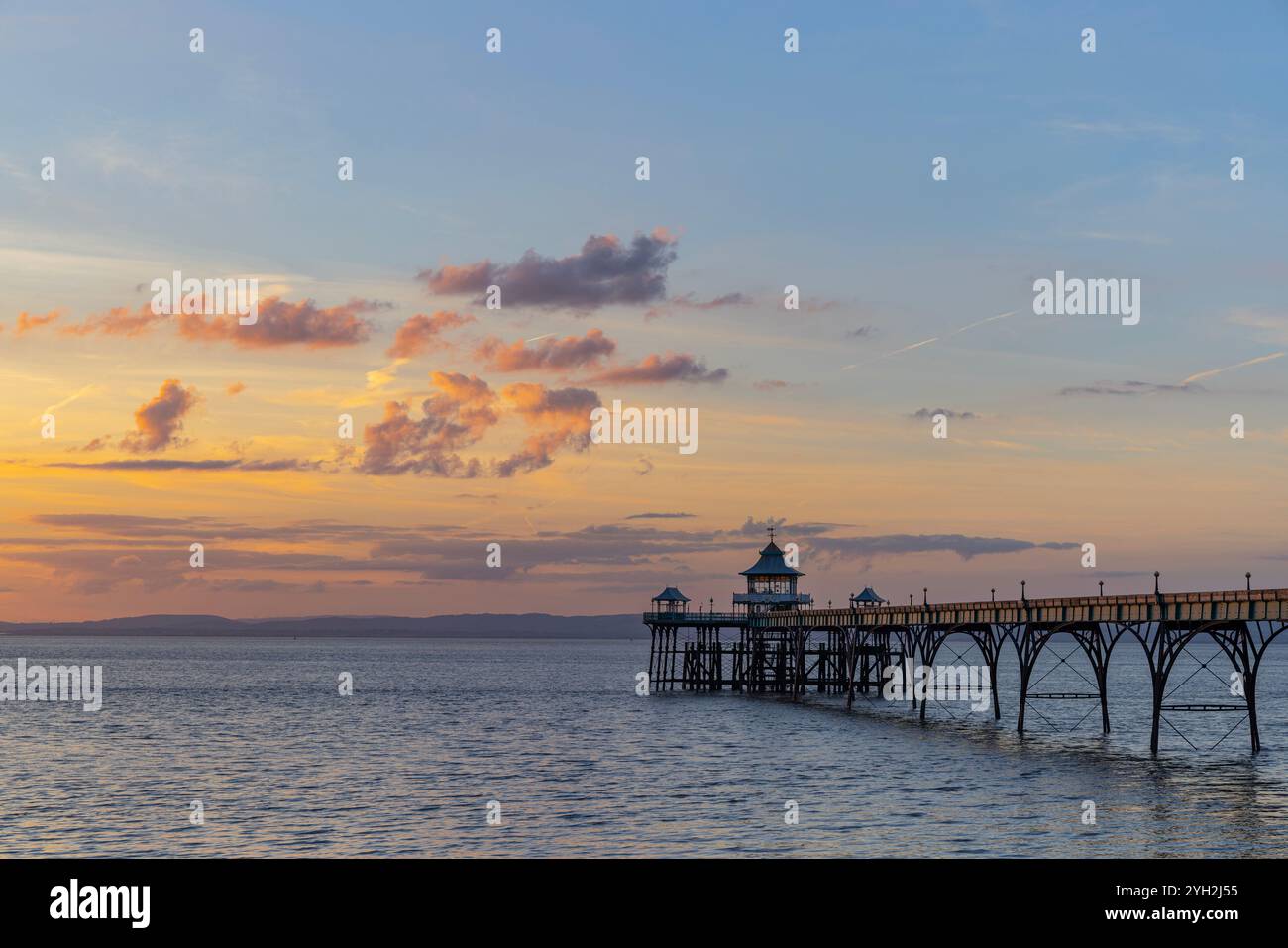 Clevedon Pier au coucher du soleil avec une couverture nuageuse et un ciel bleu avec la lumière du soleil se reflétant sur les panneaux latéraux de la jetée Banque D'Images