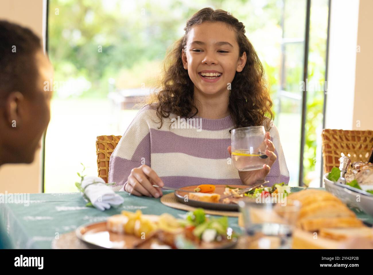 Temps de Noël, fille souriante profitant d'un repas de fête avec la famille multiraciale à la maison, tenant le verre Banque D'Images