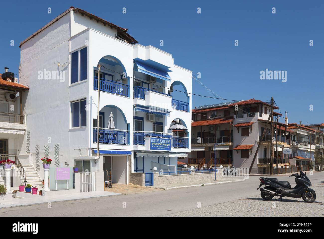 Bâtiment moderne, blanc avec balcons bleus, scooter solitaire sur la rue en face de lui par temps ensoleillé, Sarti, Sithonia, Chalcidique, Chalcidique, cent Banque D'Images