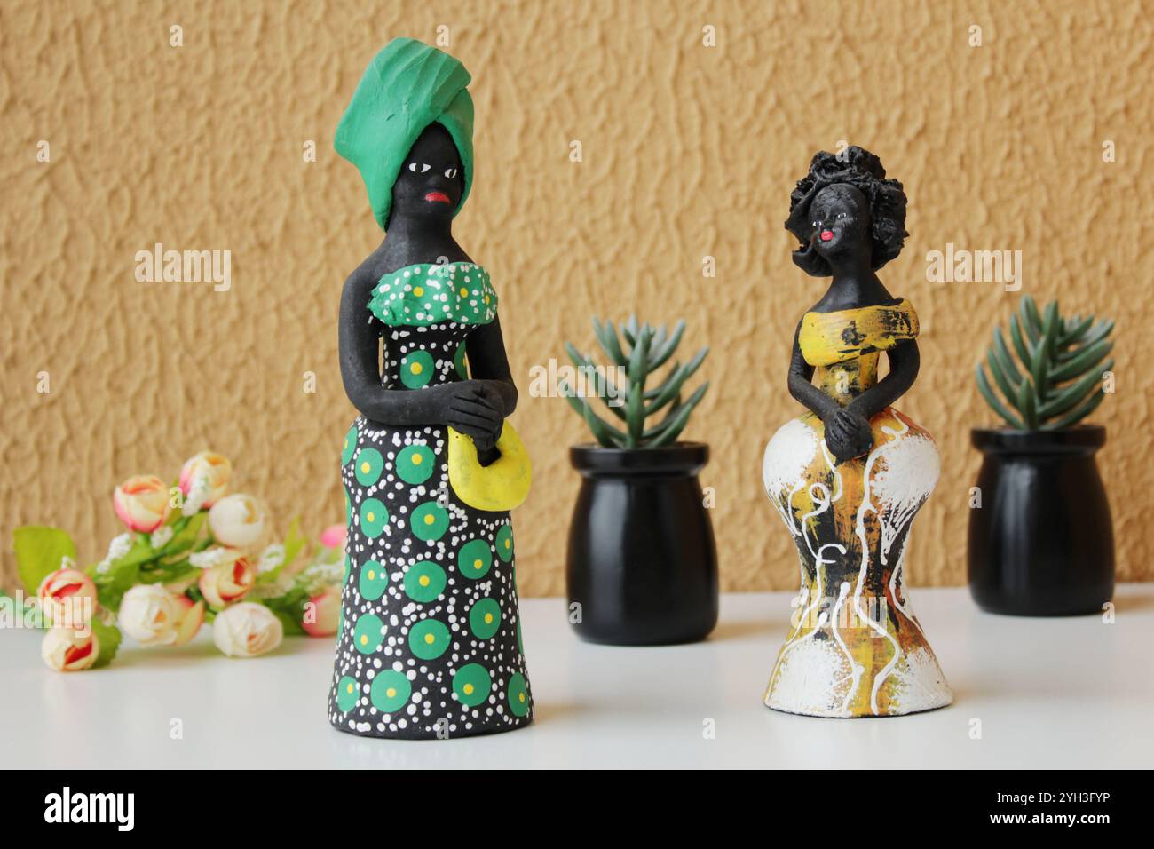 Deux statuettes de femmes noires portant des costumes traditionnels brésiliens verts et jaunes. Fond de mur de couleur orange. Vases de plantes succulentes. Banque D'Images