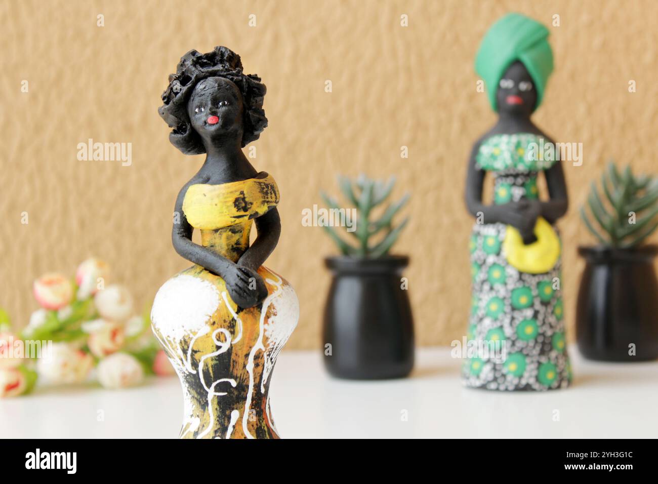 Deux statuettes de femmes noires portant des costumes traditionnels brésiliens jaunes et verts. Fond de mur de couleur orange et vases de plantes succulentes. Banque D'Images