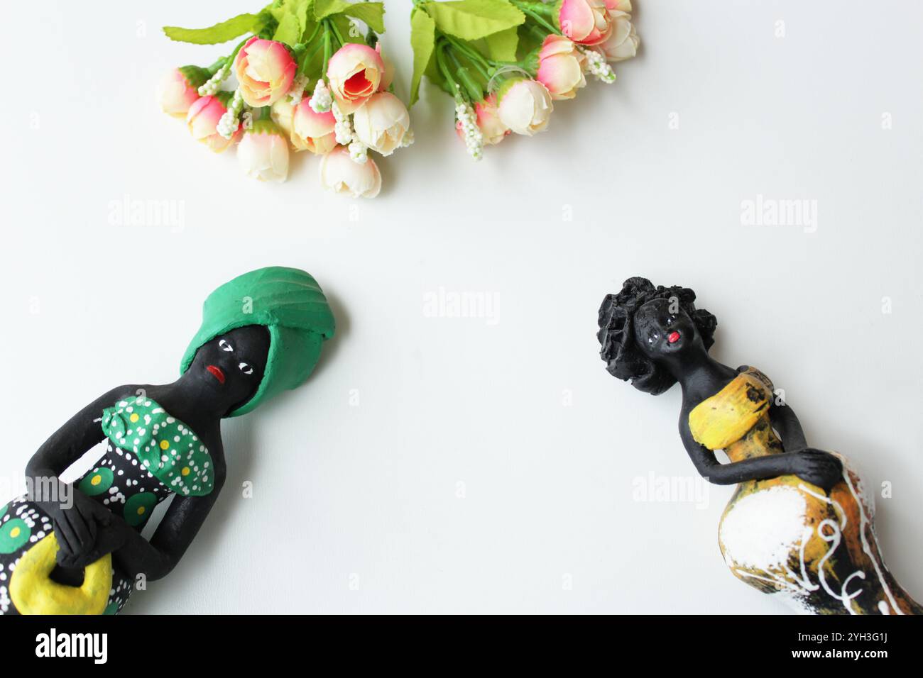 Deux statuettes de femmes noires portant des costumes traditionnels africains brésiliens et un tas de boutons roses en tissu sur fond blanc. Banque D'Images