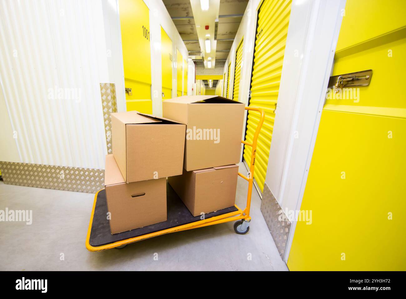 Chariot chargé de boîtes en carton dans un couloir lumineux de self-stockage. Banque D'Images