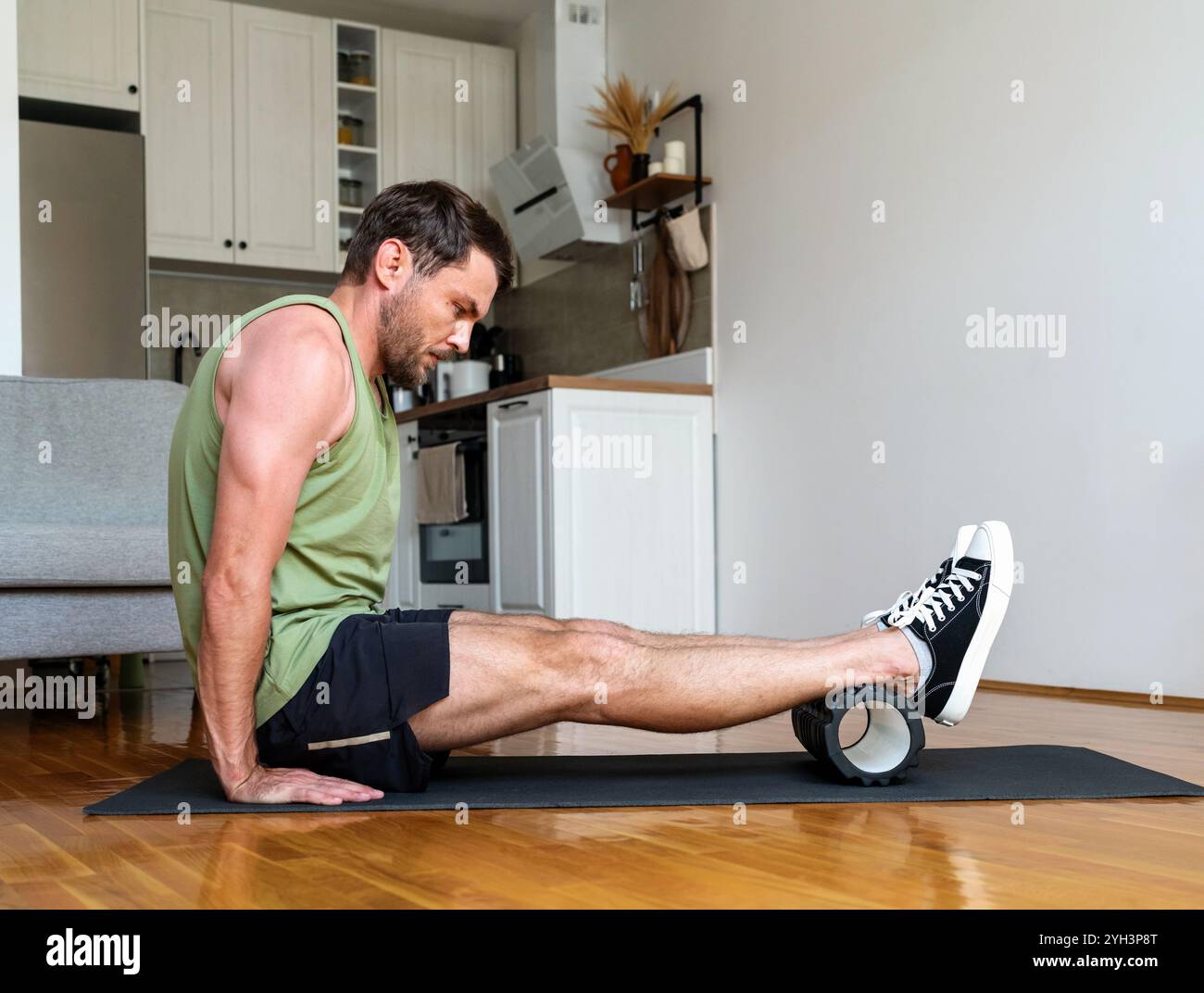 Personne masculine effectuant des exercices de libération musculaire sur un tapis de yoga avec un rouleau en mousse à la maison. Banque D'Images