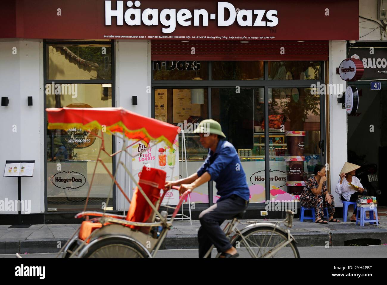 Hanoi, Vietnam - 10 juillet 2023 : un vietnamien monte son pousse-pousse devant un magasin de glaces Haagen Dazs dans un quartier touristique. Banque D'Images